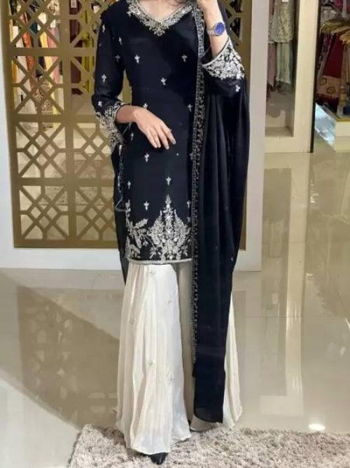 A woman modeling a black premium designer party wear set which includes a heavy chinon silk top, palazzo, and dupatta with sequin embroidery and a fancy border.